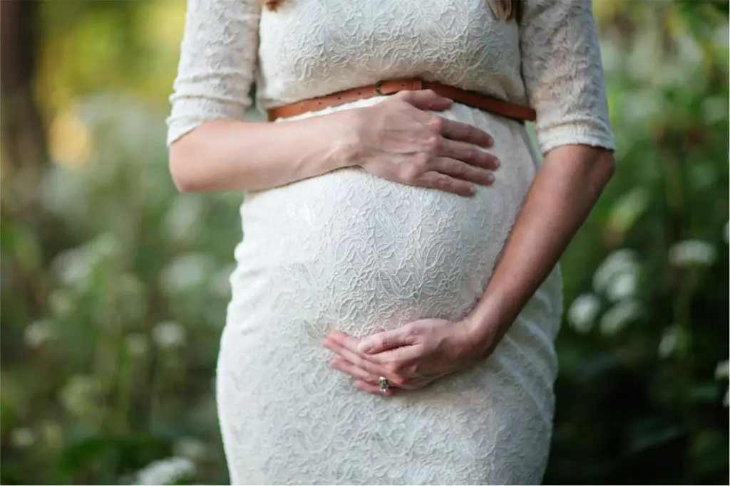 Gestante com as duas mãos na barriga de rouba branca no fundo verde